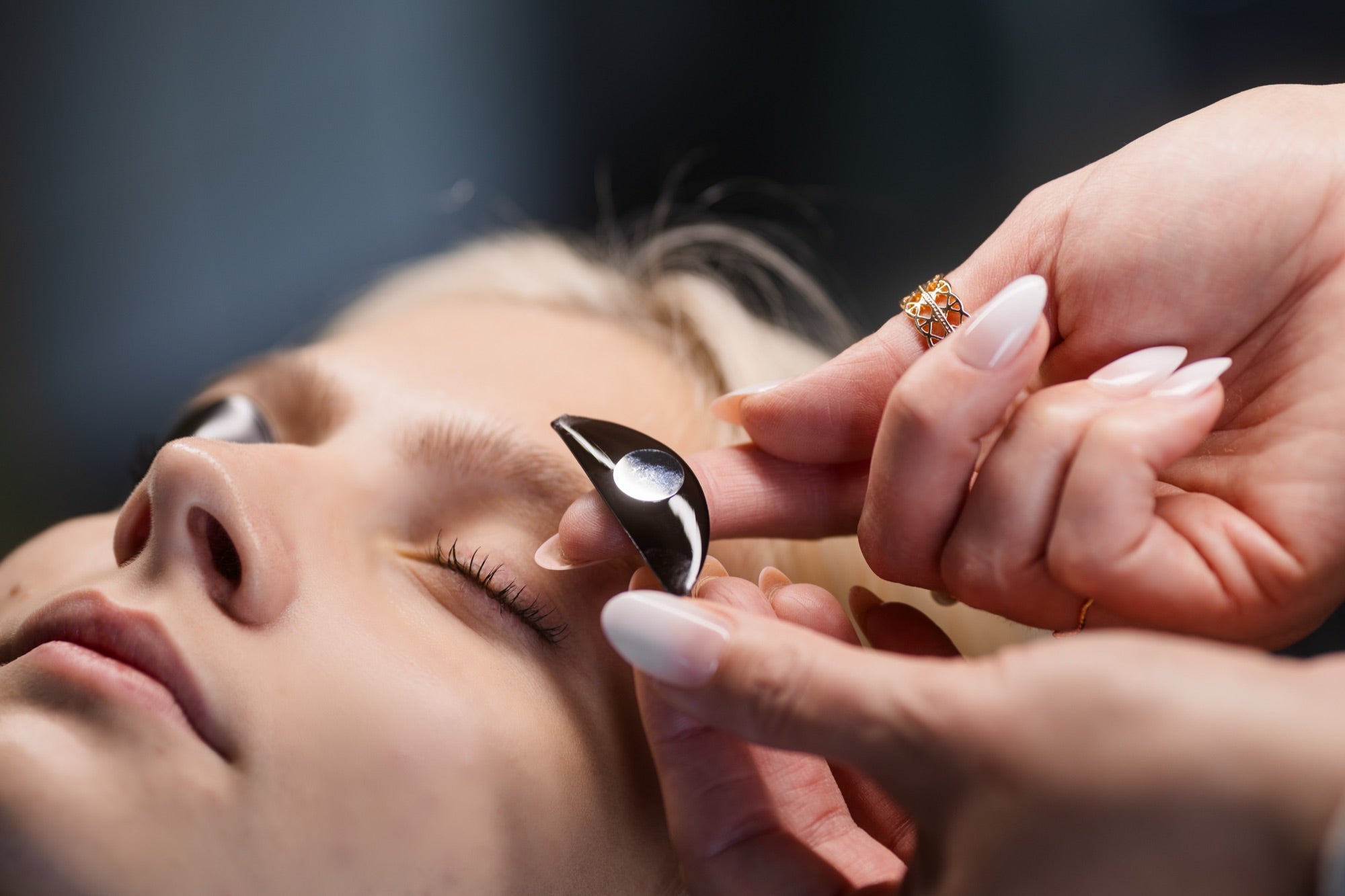 Lash artist placing Prolong Flutterstop gel pad on client eyelid - weighted disk visible